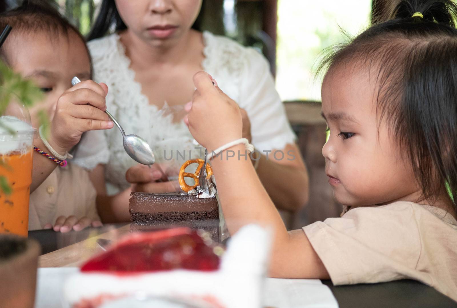 Happy Asian family are eating chocolate cake so delicious at coffee cafe in Chiang Mai. by TEERASAK
