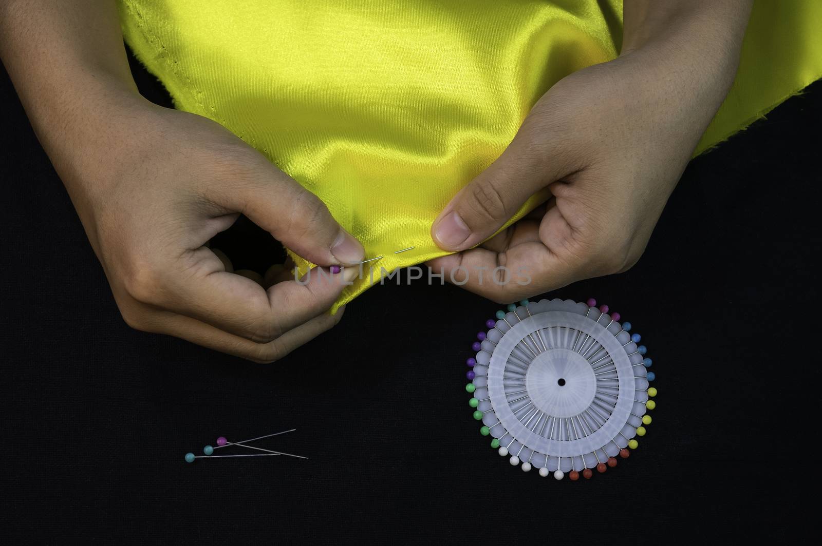 Close-up hand of Asian women are using pins to stitching before sewing over black background. by TEERASAK