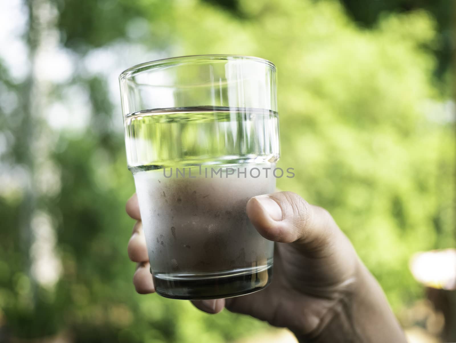 Close-up hand of woman holding cold water in clear glass over nature background.