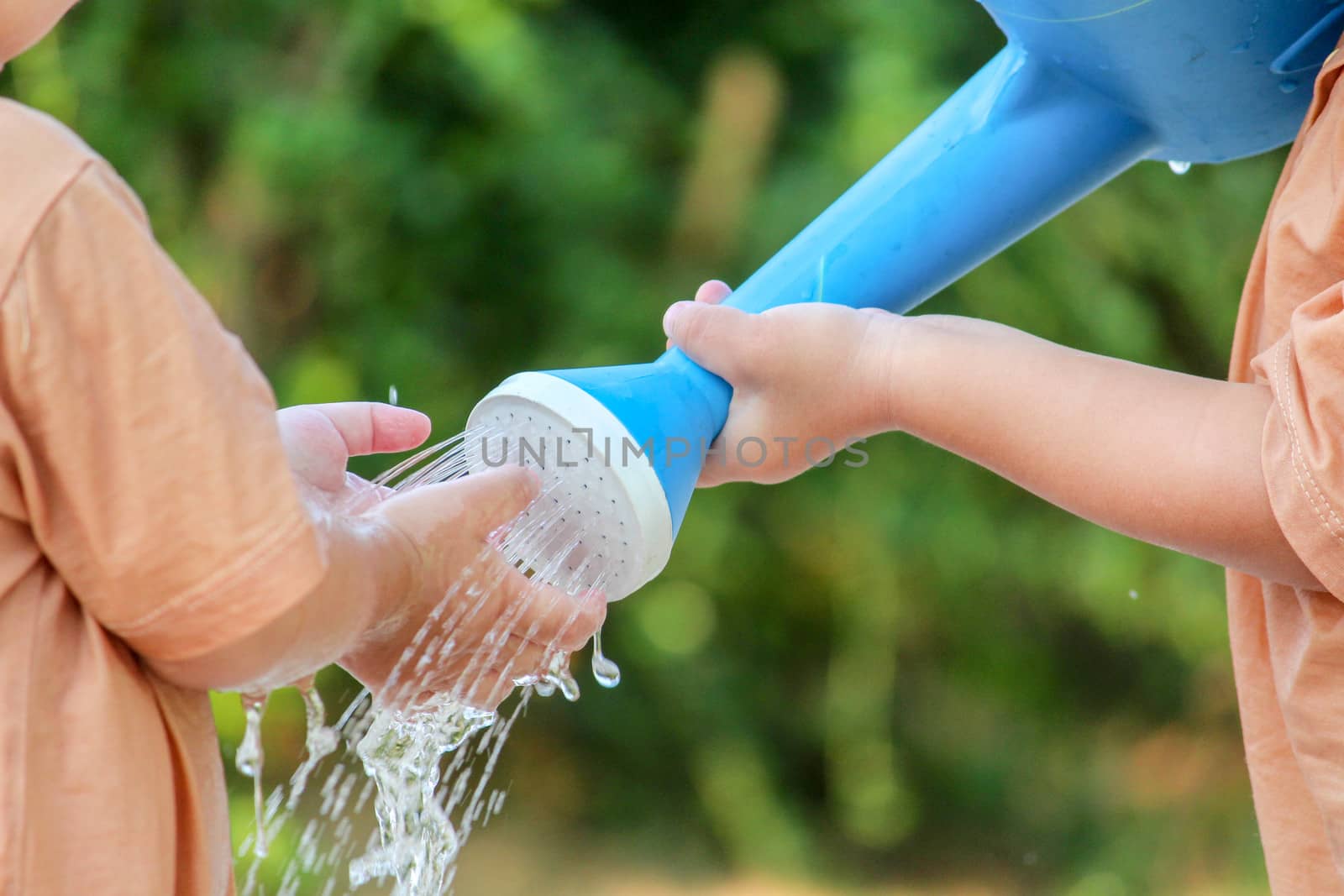 Close-up of Cute asian little child girl with sister having fun to play with water from blue watering can outside in summer garden . by TEERASAK