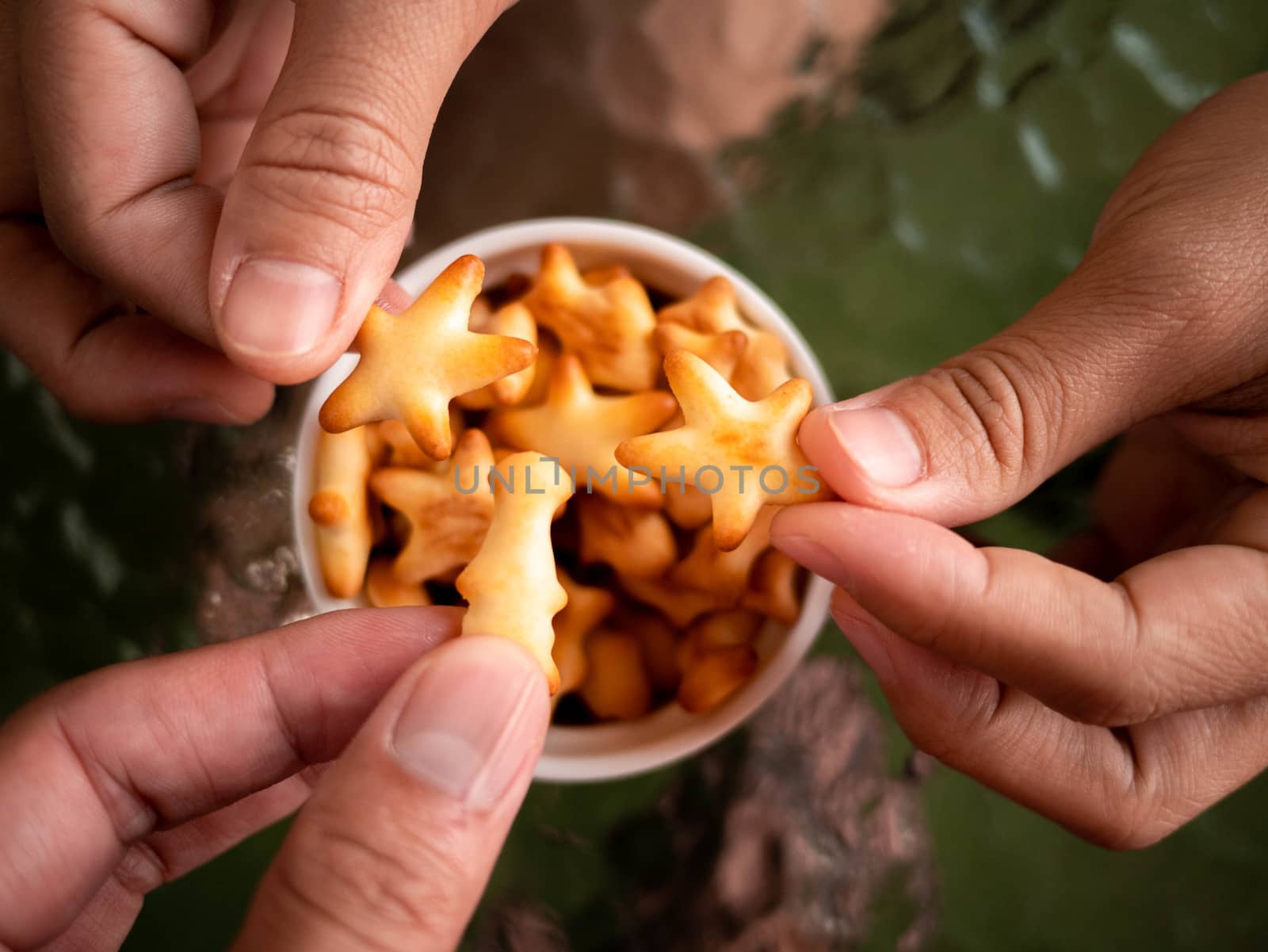 Close-up of hand hold healthy low calorie animal crackers in small cup placed on glass table.