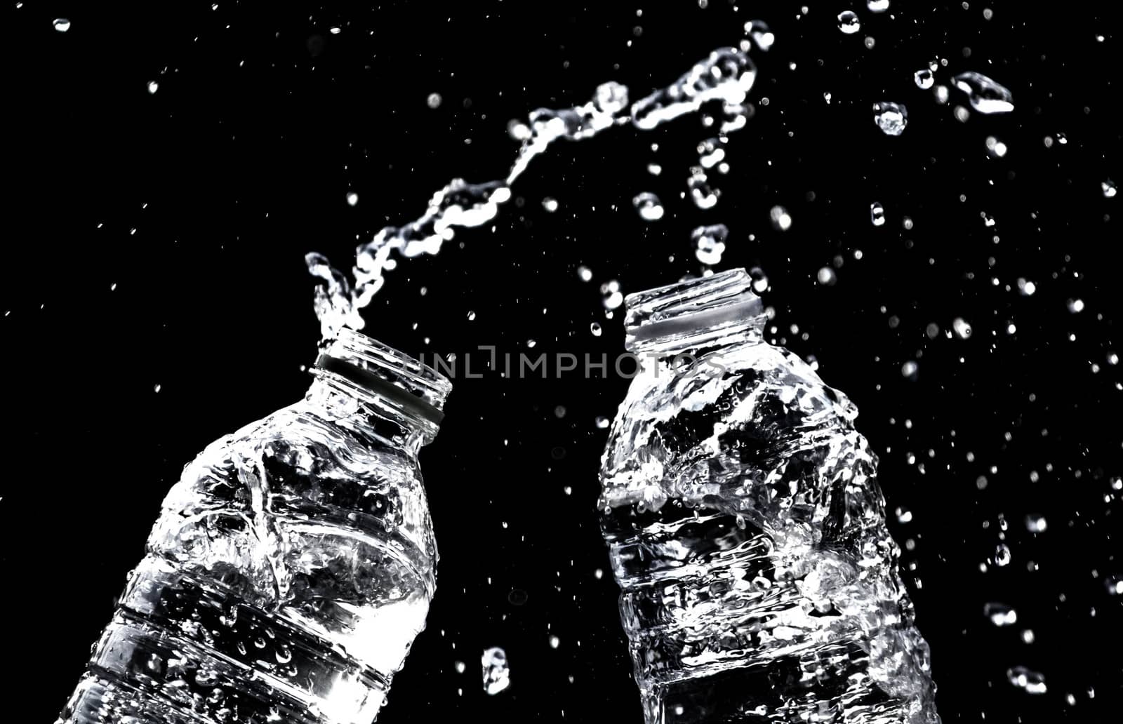 Fresh pure water splashing out of bottle on black background. Selective focus and space for text.