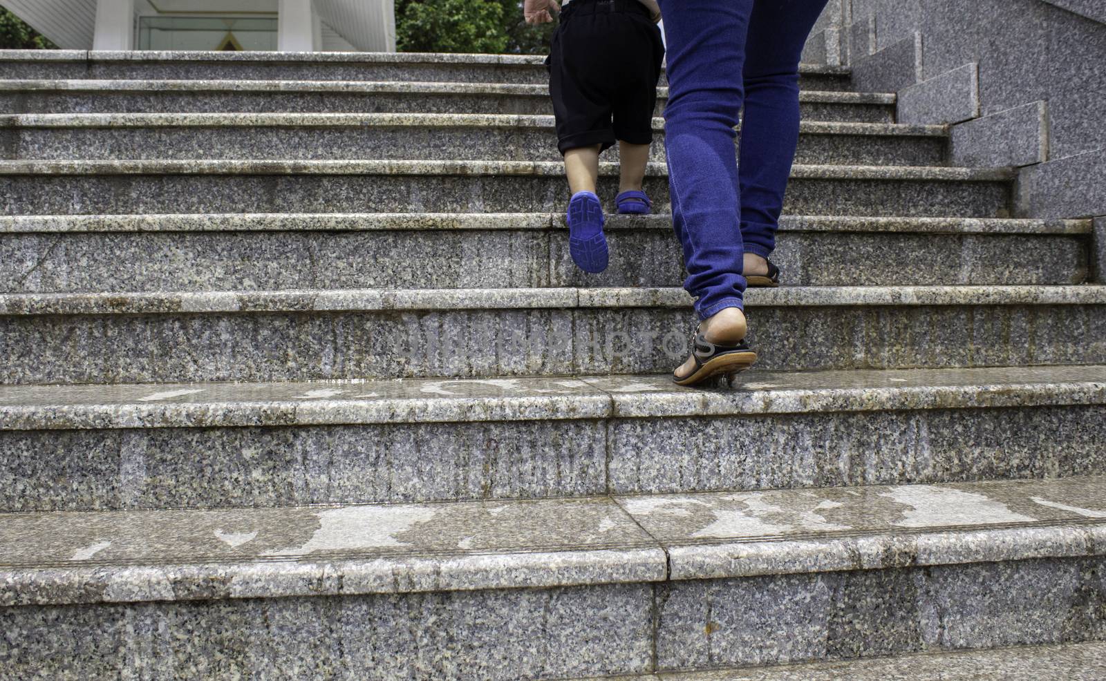 Close up of legs Asian mother and her daughter Walking up the wet ladder and without warning signs in the park. Dangerous for people. by TEERASAK