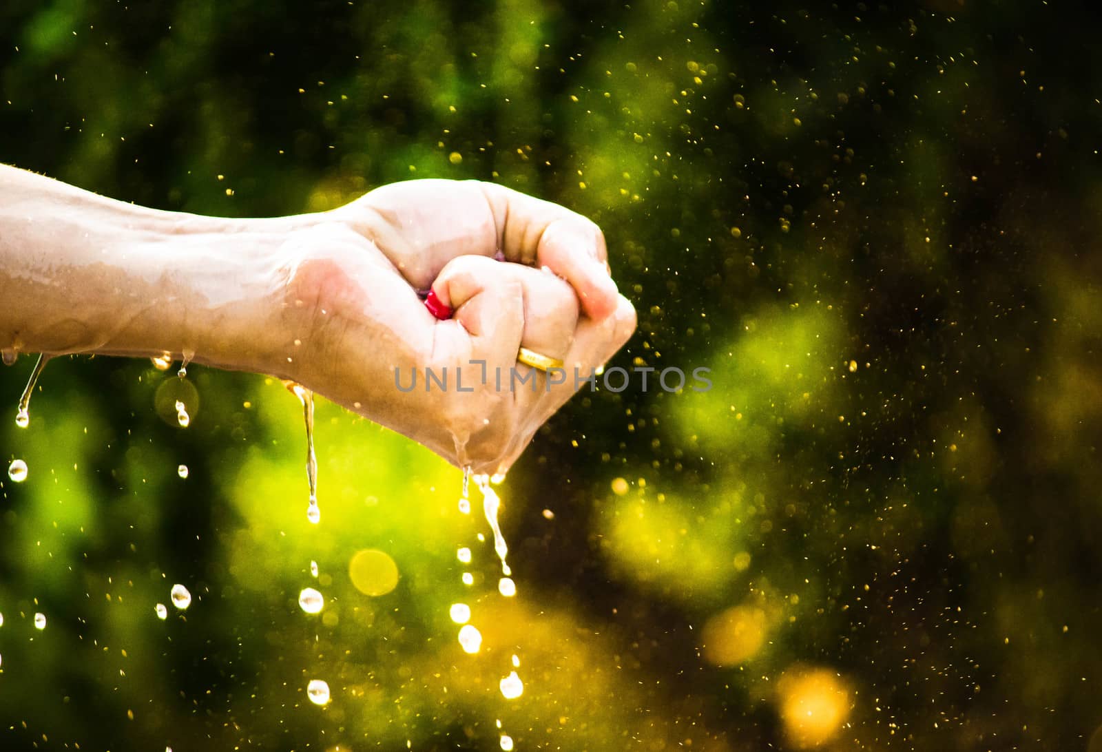 Close-up of hand squeeze the balloons that water inside and splashing around it; on blurred nature background in the garden.