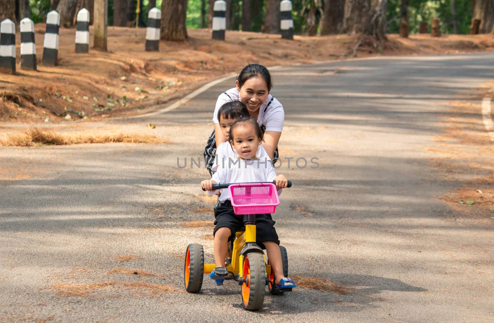 Asian young mother holding bicycle to her daughters, that riding a bicycle with her sister on the road in the garden.