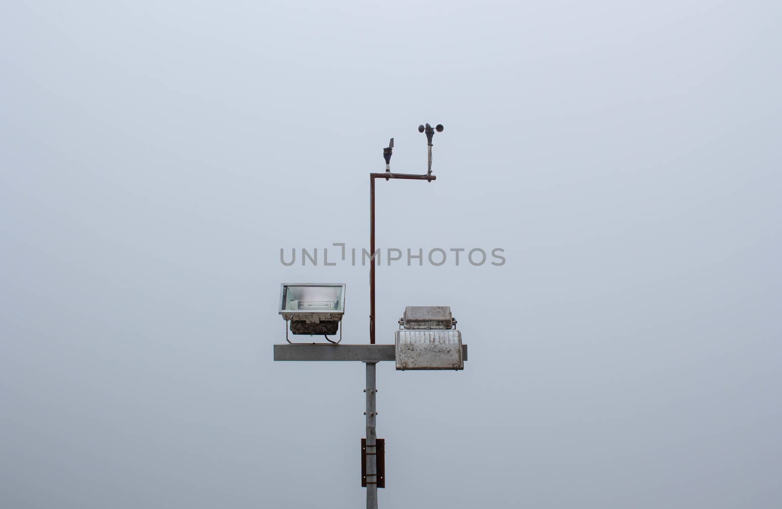 Wind force measuring device and spotlights on grey sky background.