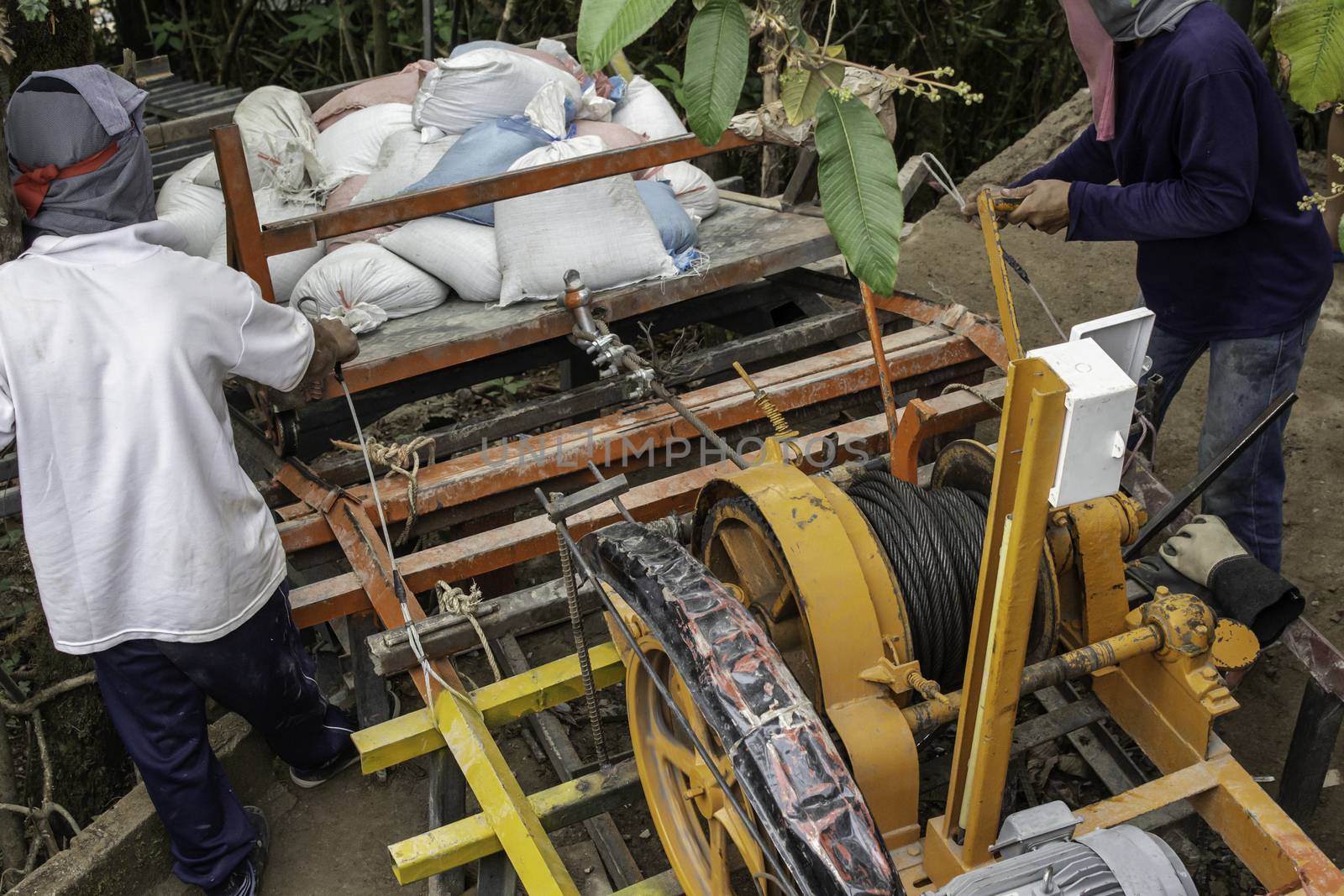 Construction workers are using electric winches to transport sandbags. by TEERASAK