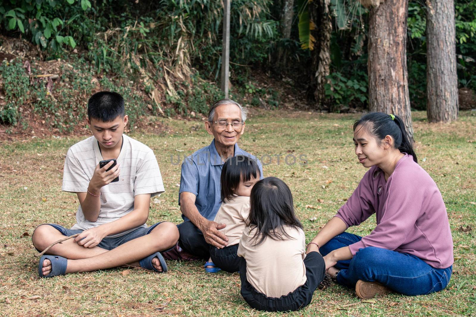 Asian family sitting on grasses ground in the garden for relaxation in summer day.