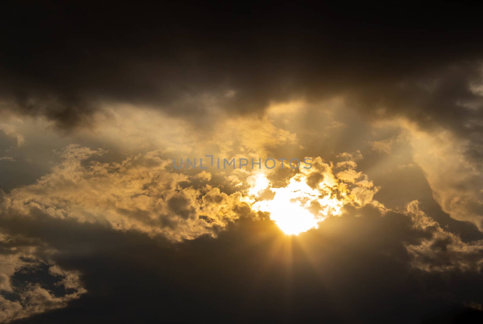 The Dark gray dramatic sky with sunlight through large clouds in rainy seasons. by TEERASAK