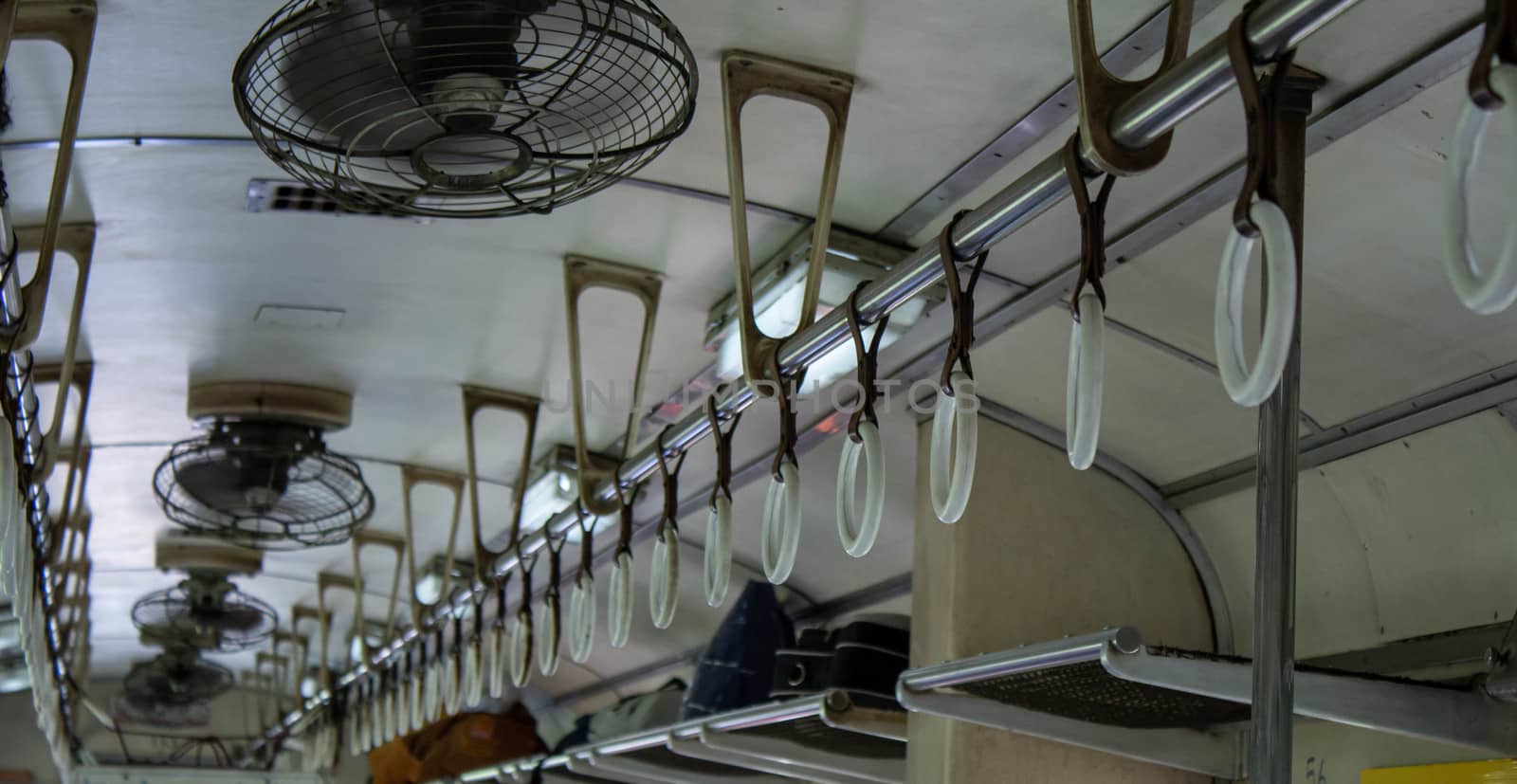 Close-up of Hand holding strap and Old fan  in the vintage diesel engine train of Thailand. by TEERASAK