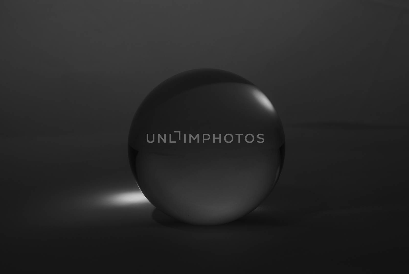 Crystal glass ball sphere transparent on dark grey gradient background.