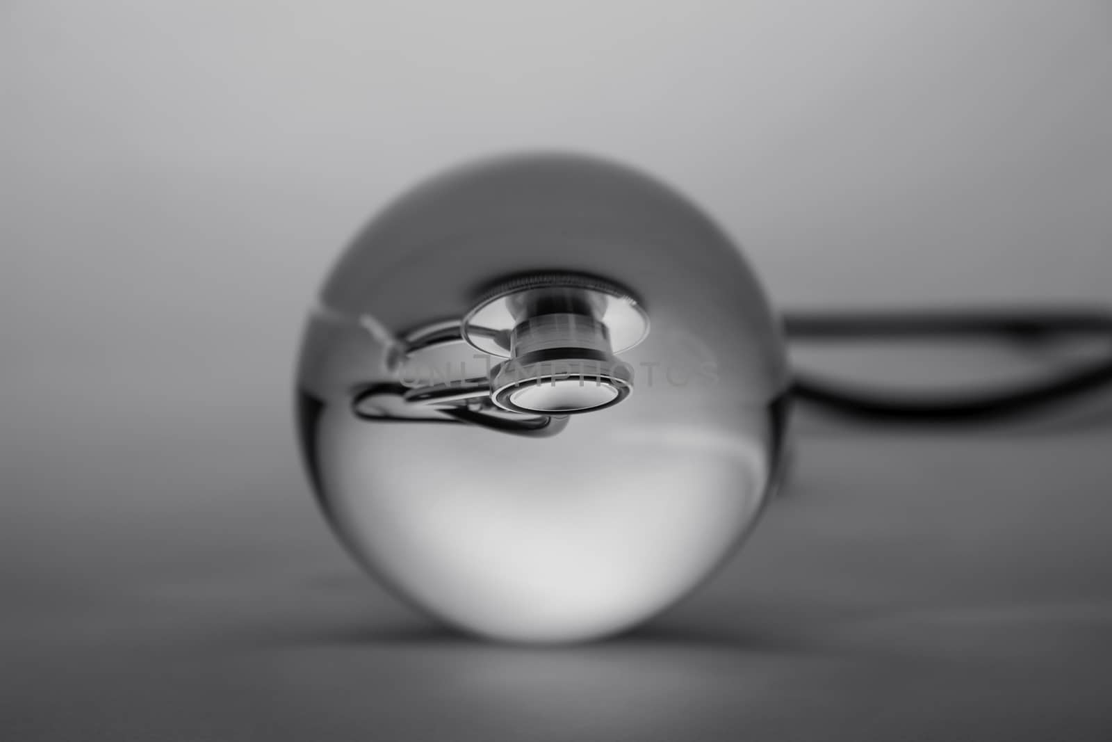 Crystal glass ball sphere revealing the inner medical stethoscope on grey gradient background. by TEERASAK