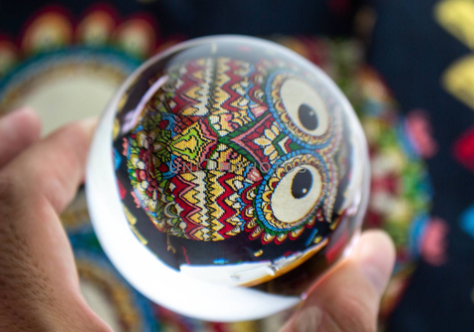 Close-up of Hand holding Crystal glass ball sphere revealing the inner Owl embroidery pattern.