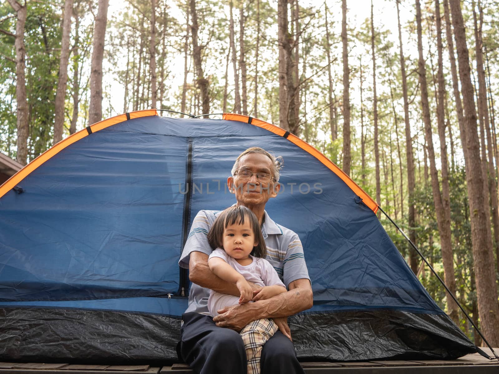 Asian Grandfather and child girl sit at the Camping page in the midst of nature. by TEERASAK