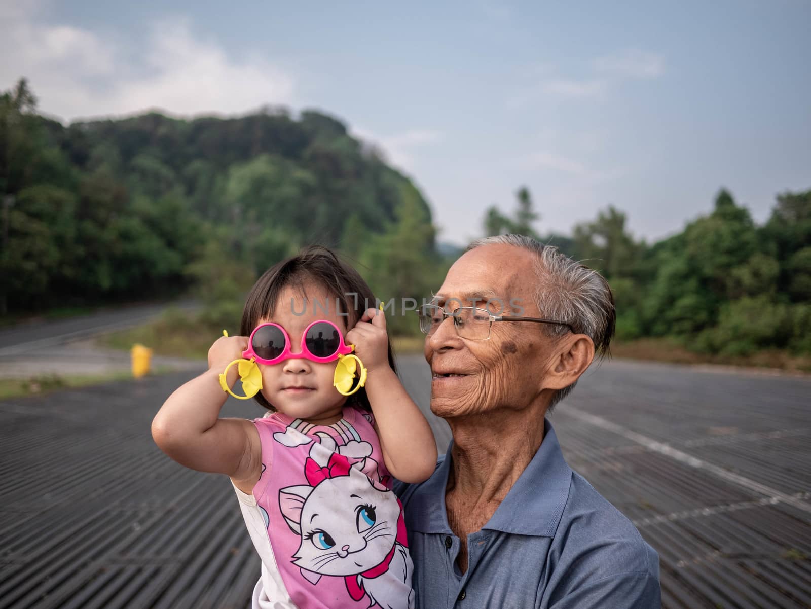 Asian grandfather carrying grandchild while her wearing pink glasses and smile. by TEERASAK