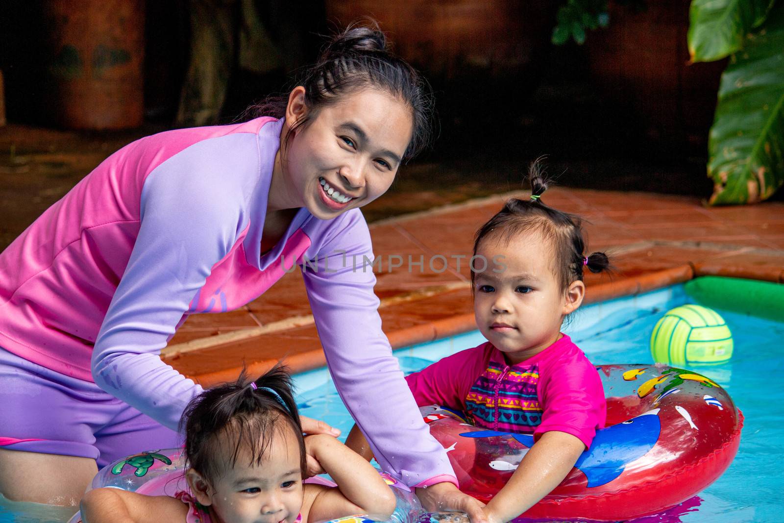 Young Asian mother and her daughter having fun in swimming pool.