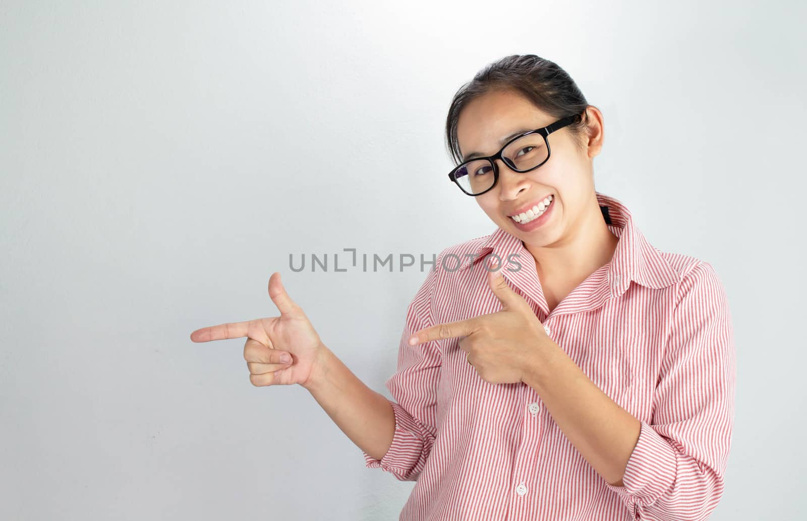 Asian woman wearing pink shirt and eyeglasses isolated on white background smiling and looking at the camera pointing with two hands and fingers to the side. by TEERASAK