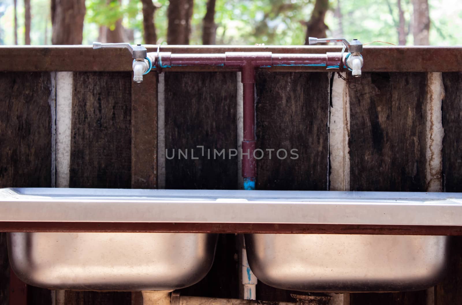 Faucet with water drop into the stainless steel sink on nature background at pine forest. Save water concept.