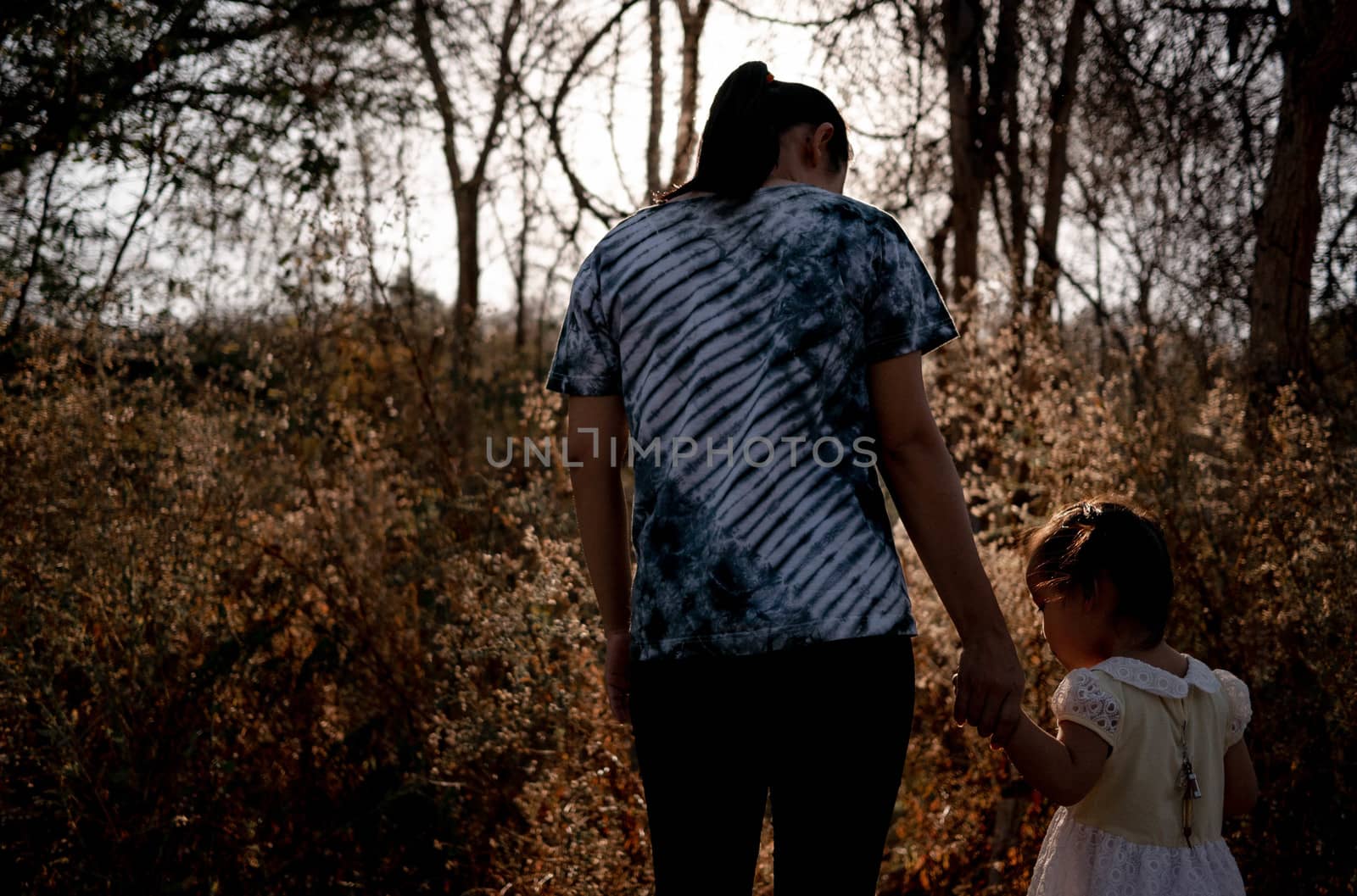 Asian mom and daughter holding hand together and stand looking view of sunset at the park. by TEERASAK