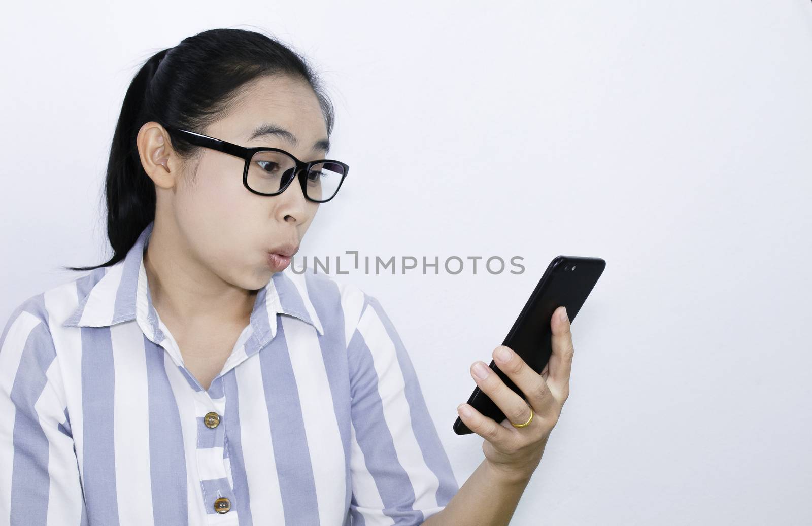 Business Asian young woman waring glasses looking smartphone over white background, shocked face. Health and medical concept. Space for text. by TEERASAK
