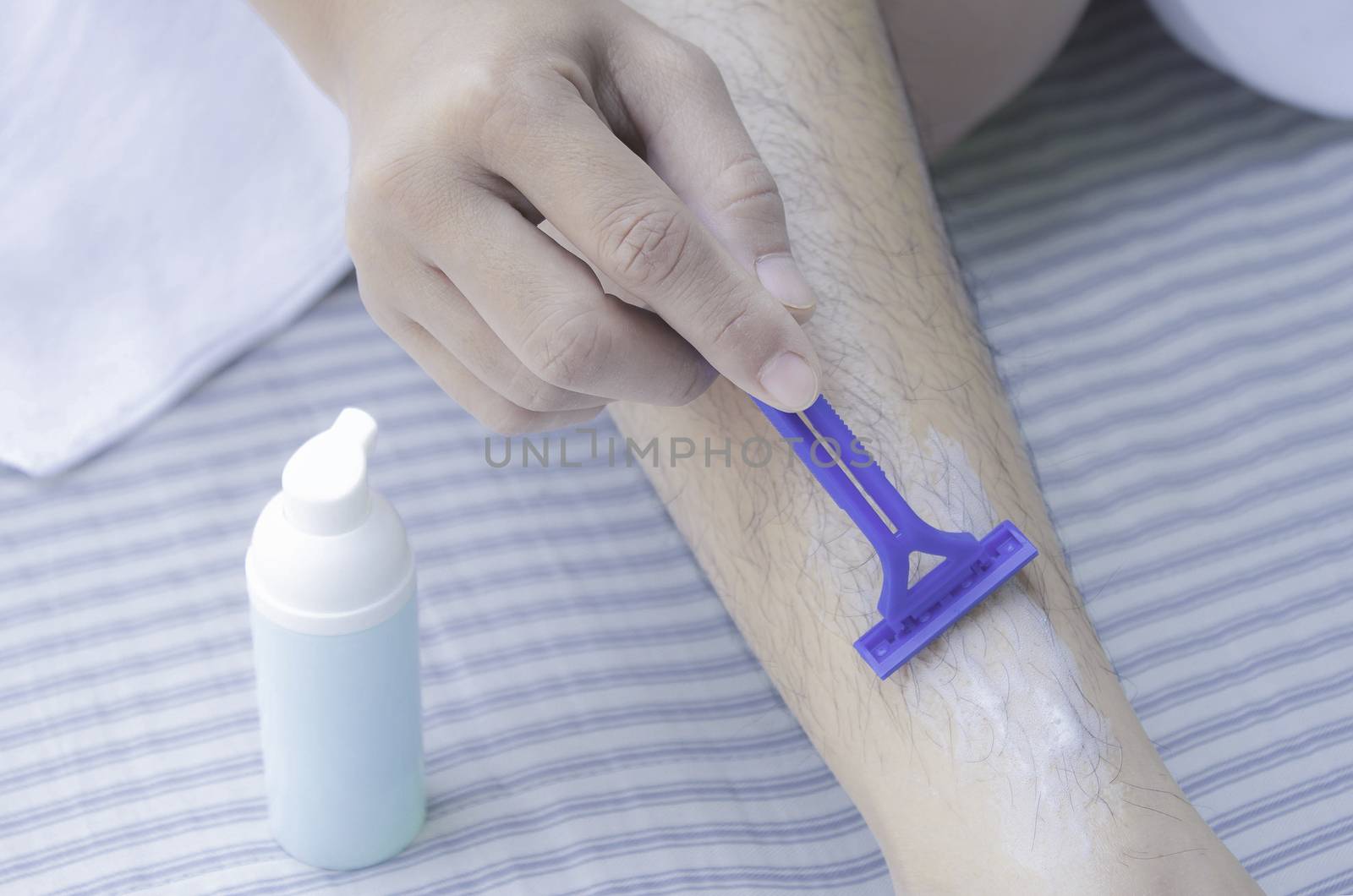 Close-up view of Asian woman shaving leg hair with blue razor and use foam to prevent injury. Body care and  Hair removal concept.