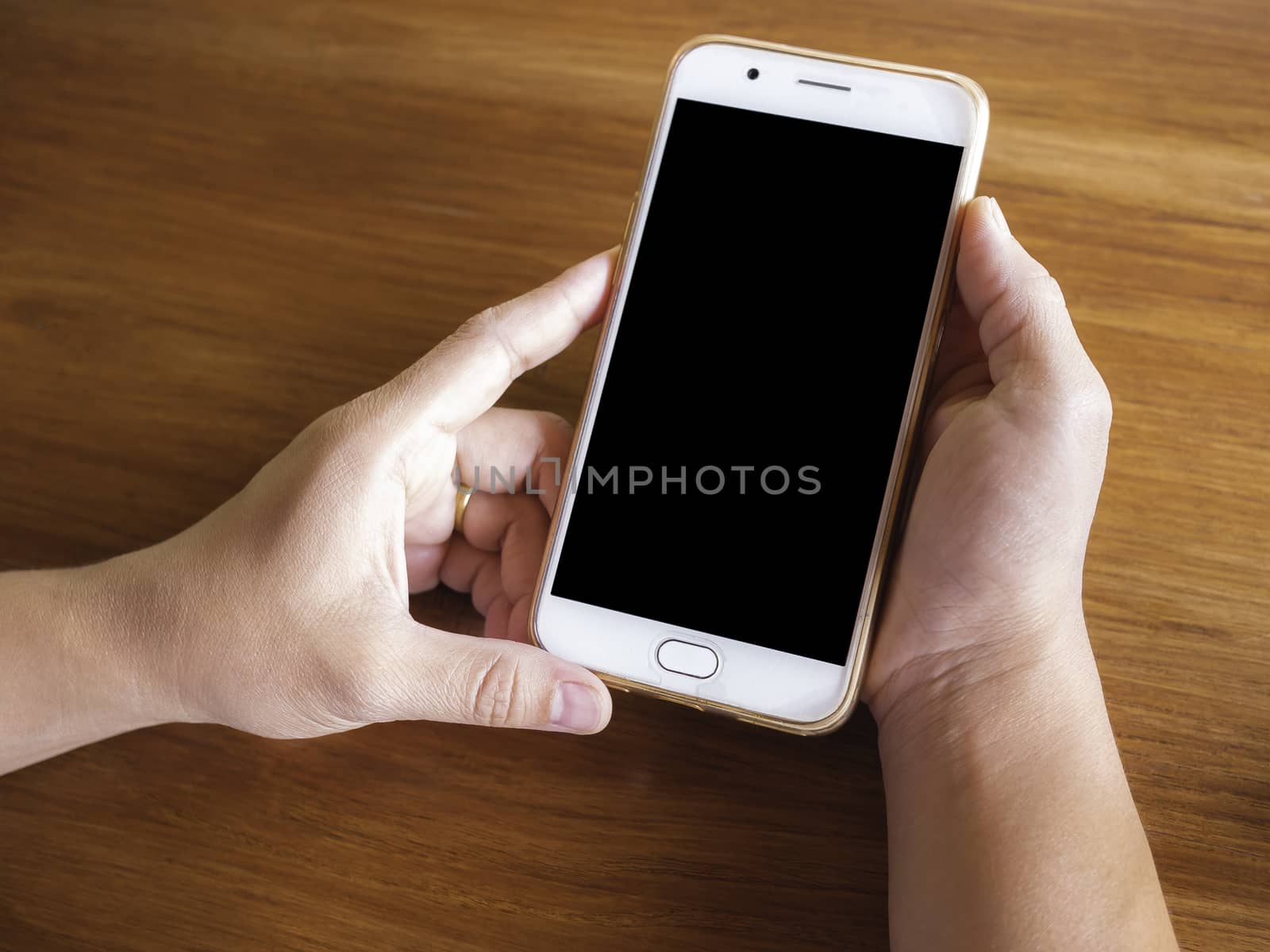 Close up of hand holding smartphone over wooden table background by TEERASAK