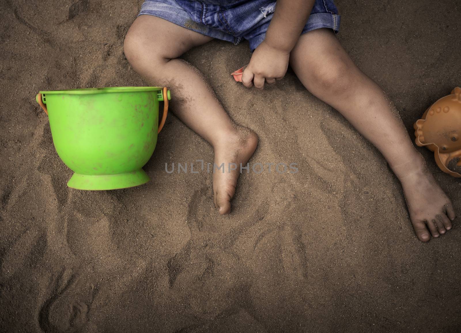 Close up of legs Asian little girl sitting on sand ground in the playground and play a sand with plastic beach toys happily. Playing is learning for children.