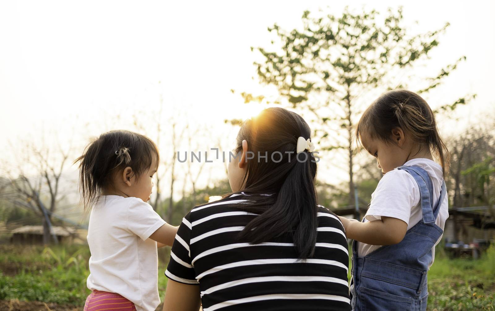 Asian little child girl drink water from bottle after tired of playing in the garden with mother and sister, looking sunset in evening.