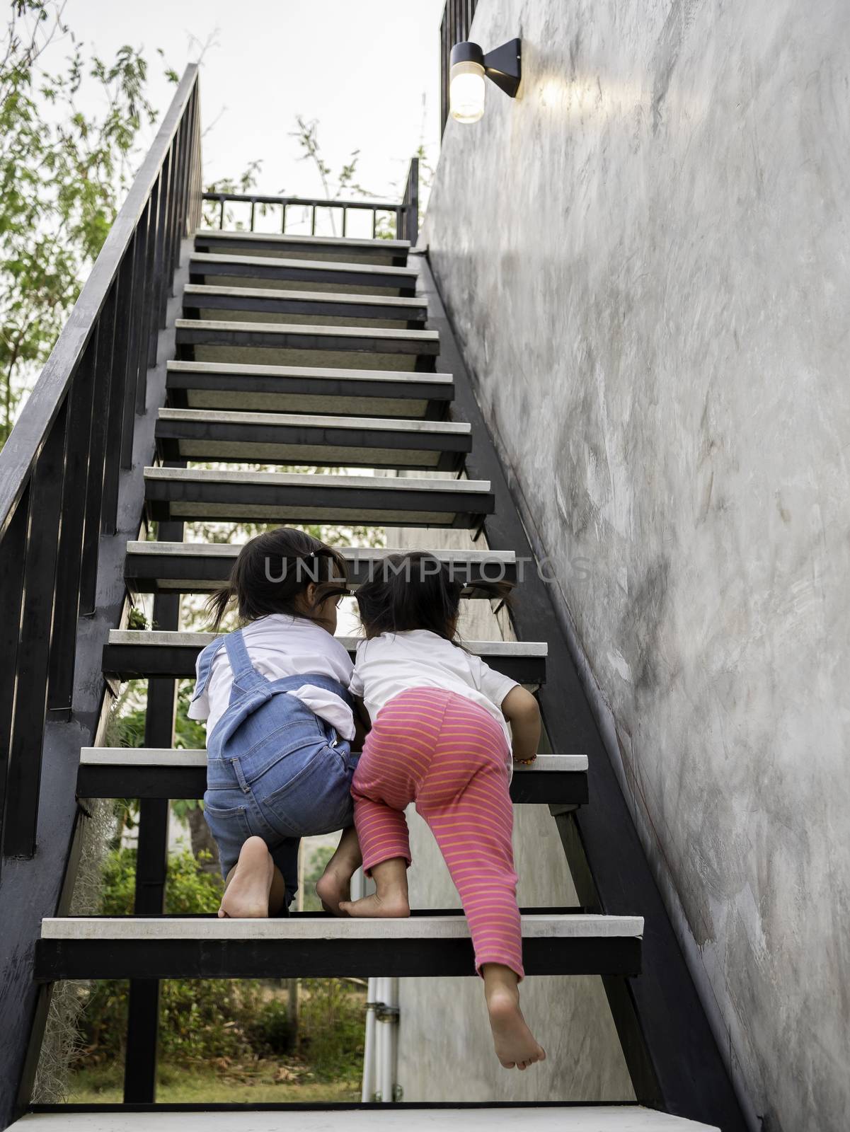 Asian little girl and her sister try to climb the stairs together. Dangerous in children. Education and self-development concept.