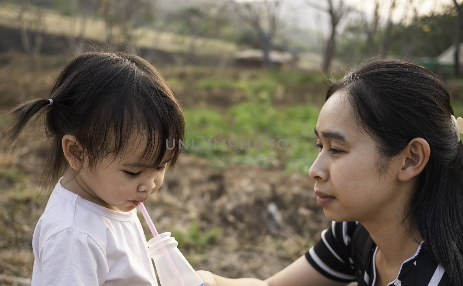 Asian little child girl drink water from tube after tired of playing in the garden with mother. by TEERASAK