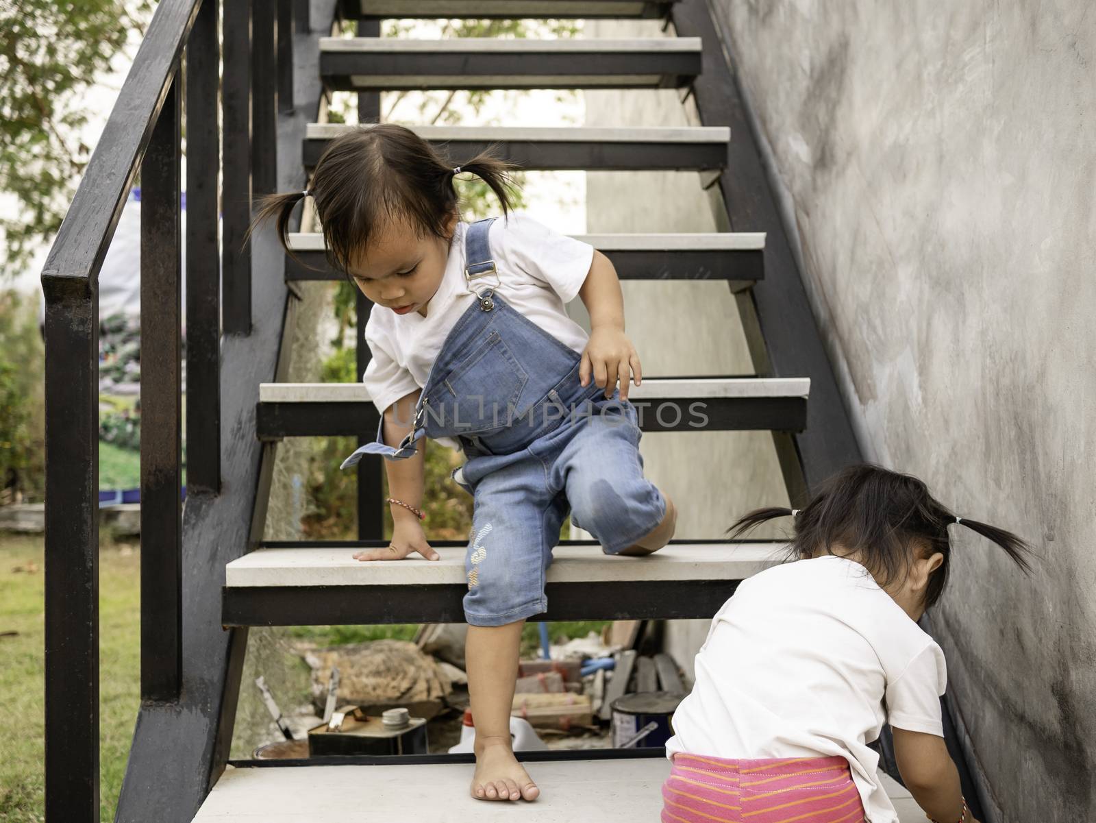 Asian little child and sister try to climb the stairs by herself. Dangerous in children. Education and self-development concept. by TEERASAK