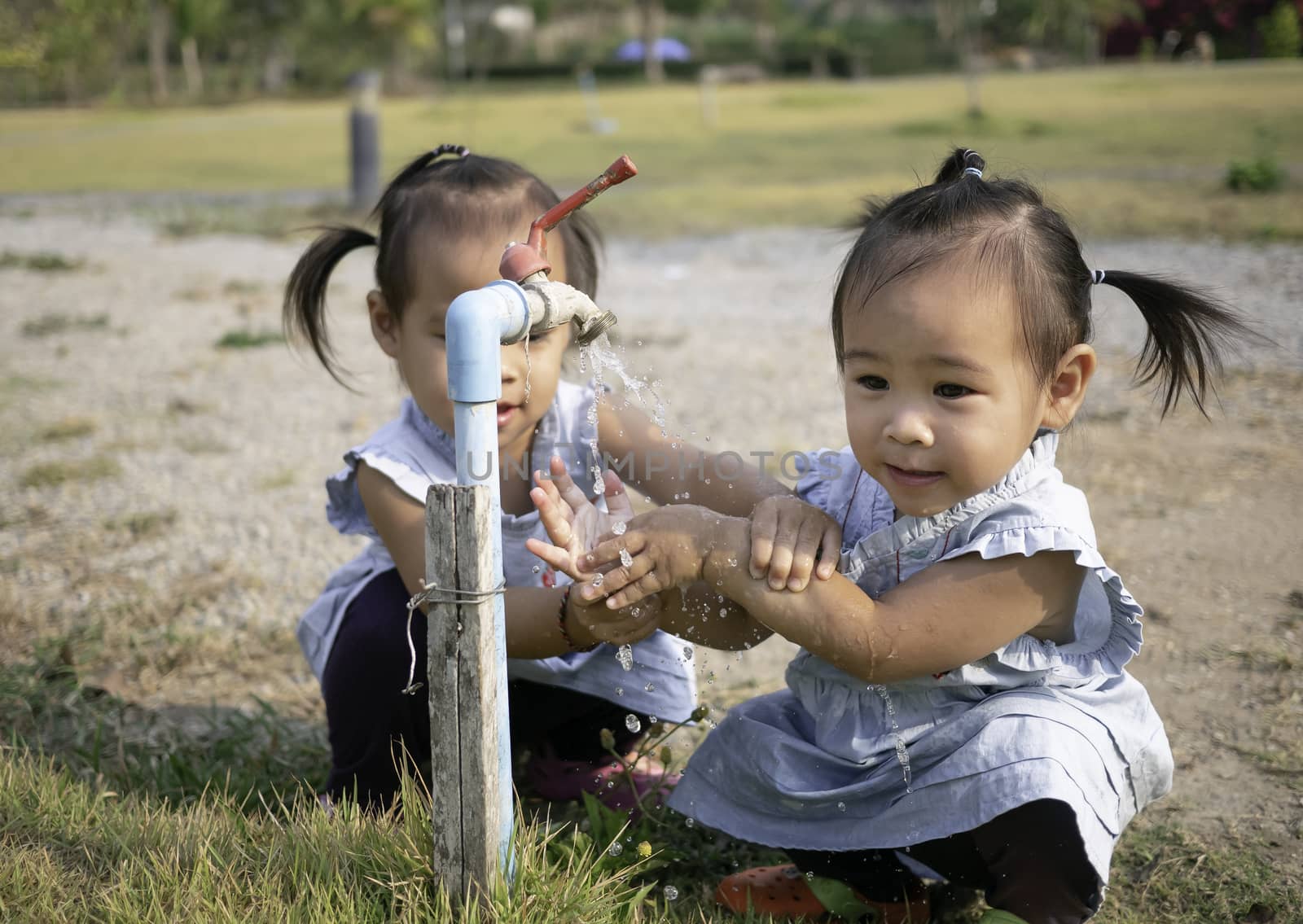 Asian little girl and sister washing her hands from steel faucets in the garden. by TEERASAK