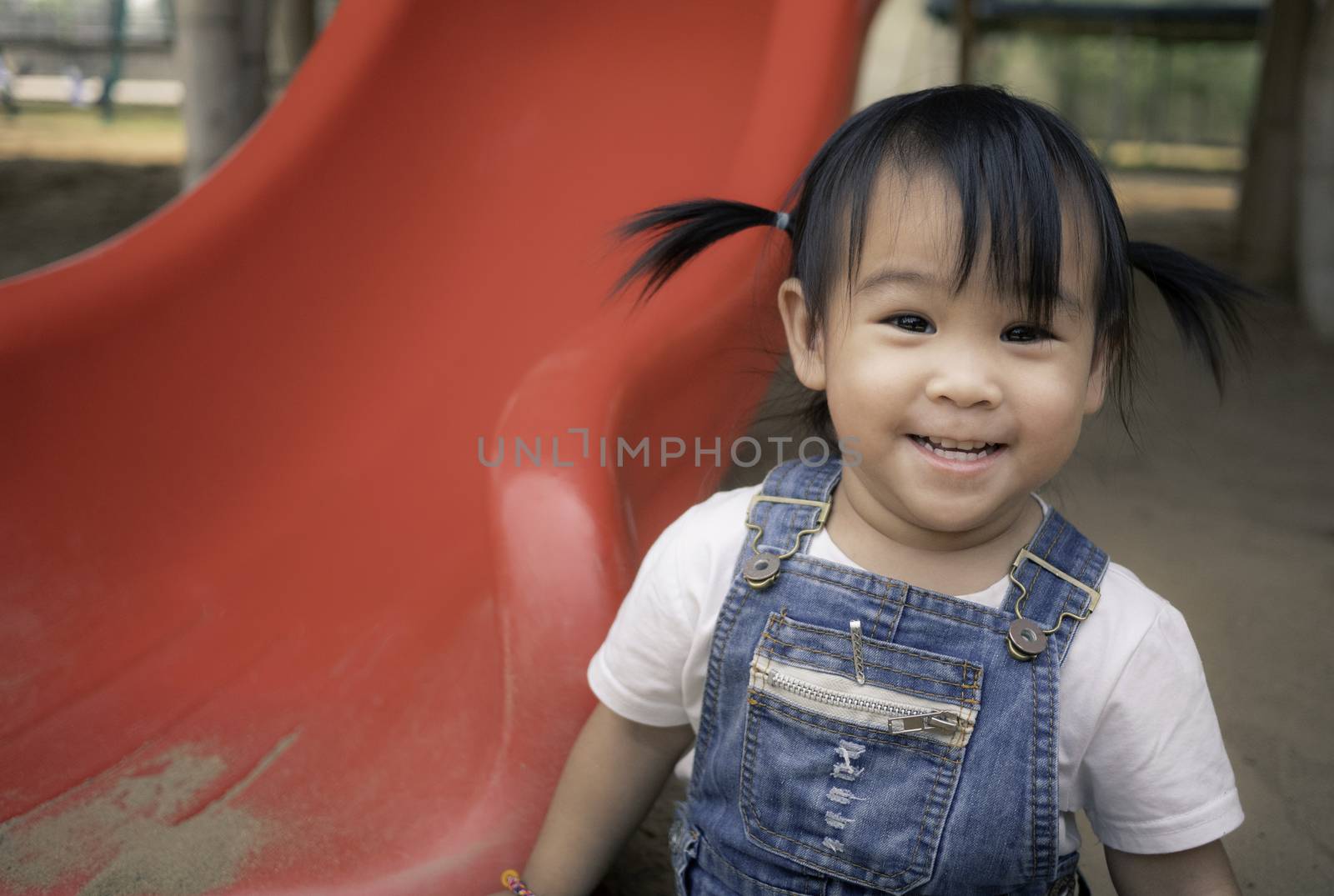 Asian little girl sitting on the sand ground in the playground and playing a sand with smile happily. Playing is learning for children. by TEERASAK