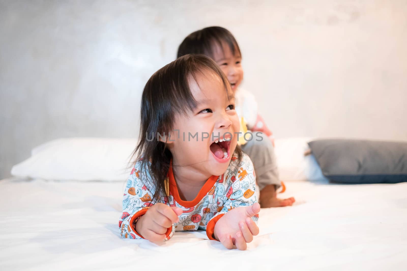 Asian little girl sitting on the back of her elderly sister and laughed together happily in the hotel room in Chiang Mai, Thailand.
