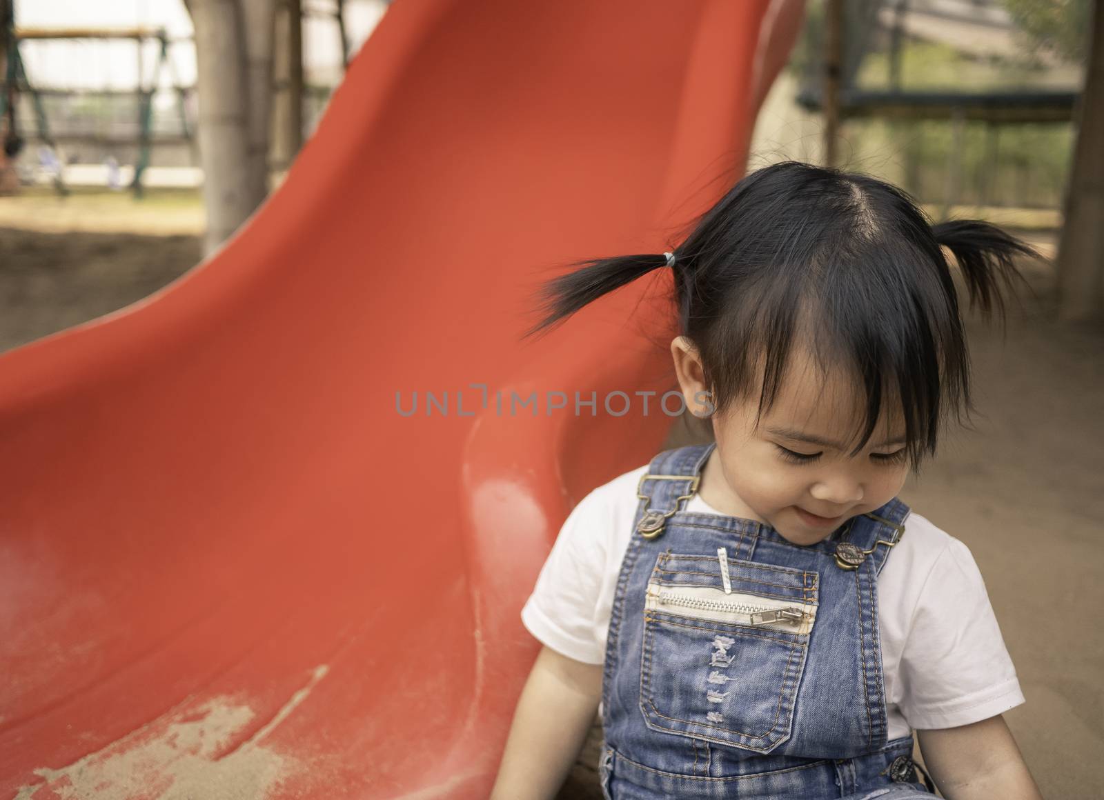 Asian little girl sitting on the sand ground in the playground and playing a sand with smile happily. Playing is learning for children.