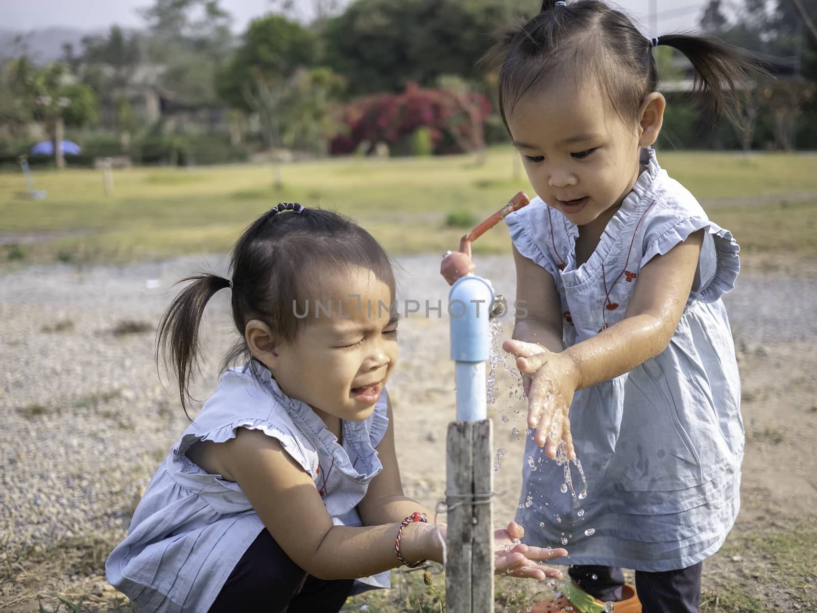 Asian little girl and sister washing her hands from steel faucets in the garden. by TEERASAK
