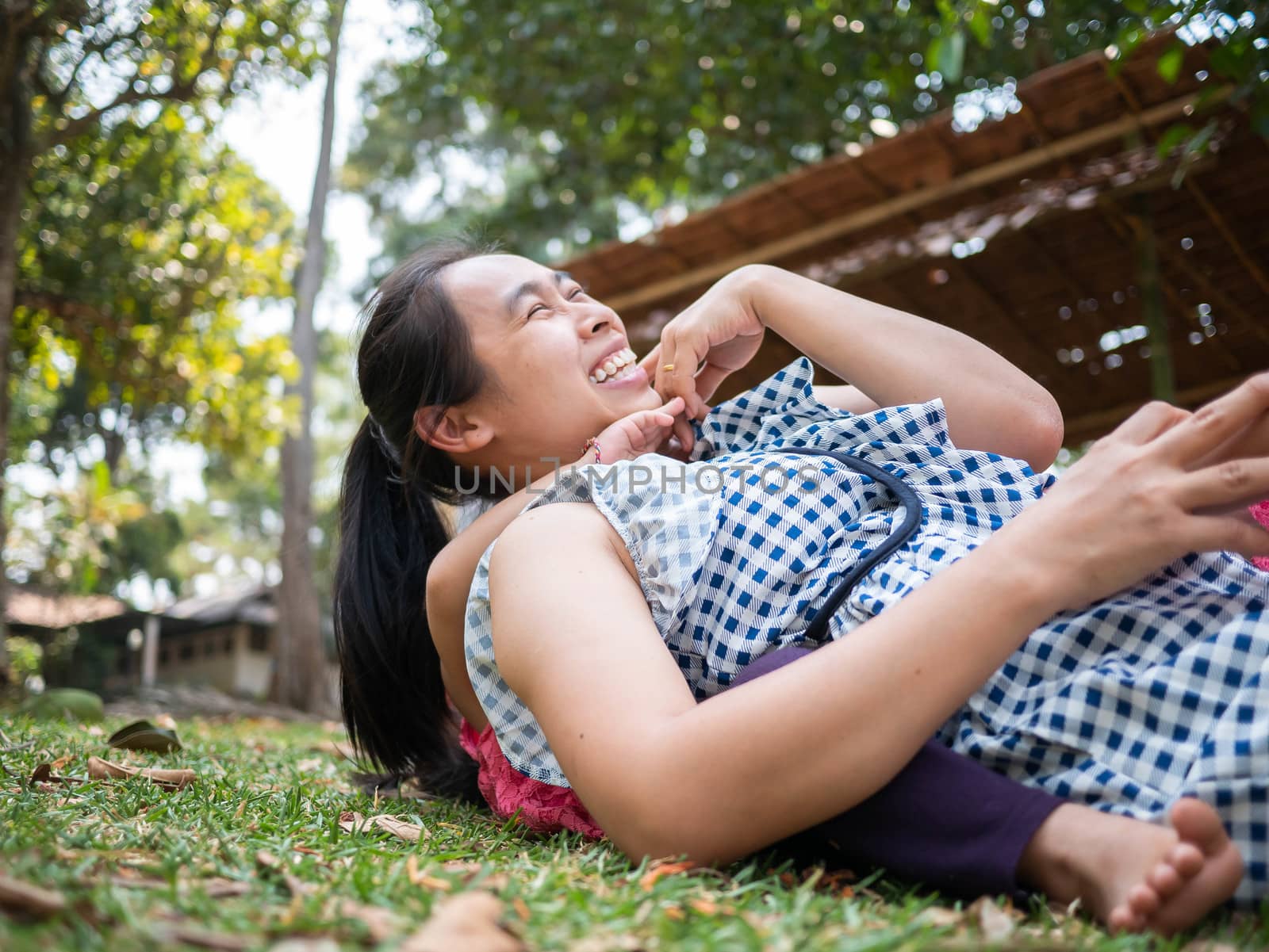 Asian little girl hugging her mother from the back; Pretend mother while lying on grass in the park.