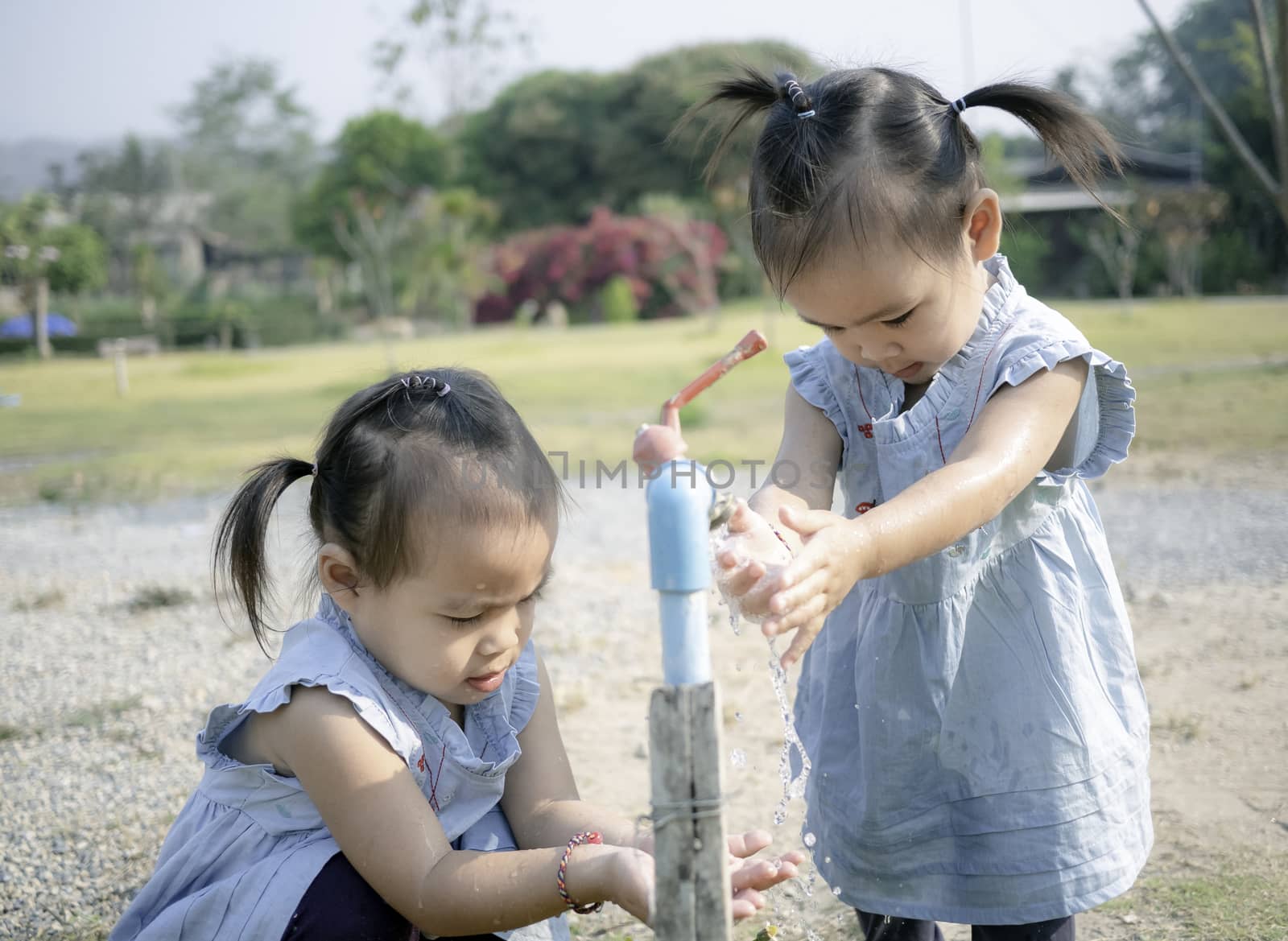 Asian little girl and sister washing her hands from steel faucets in the garden. by TEERASAK