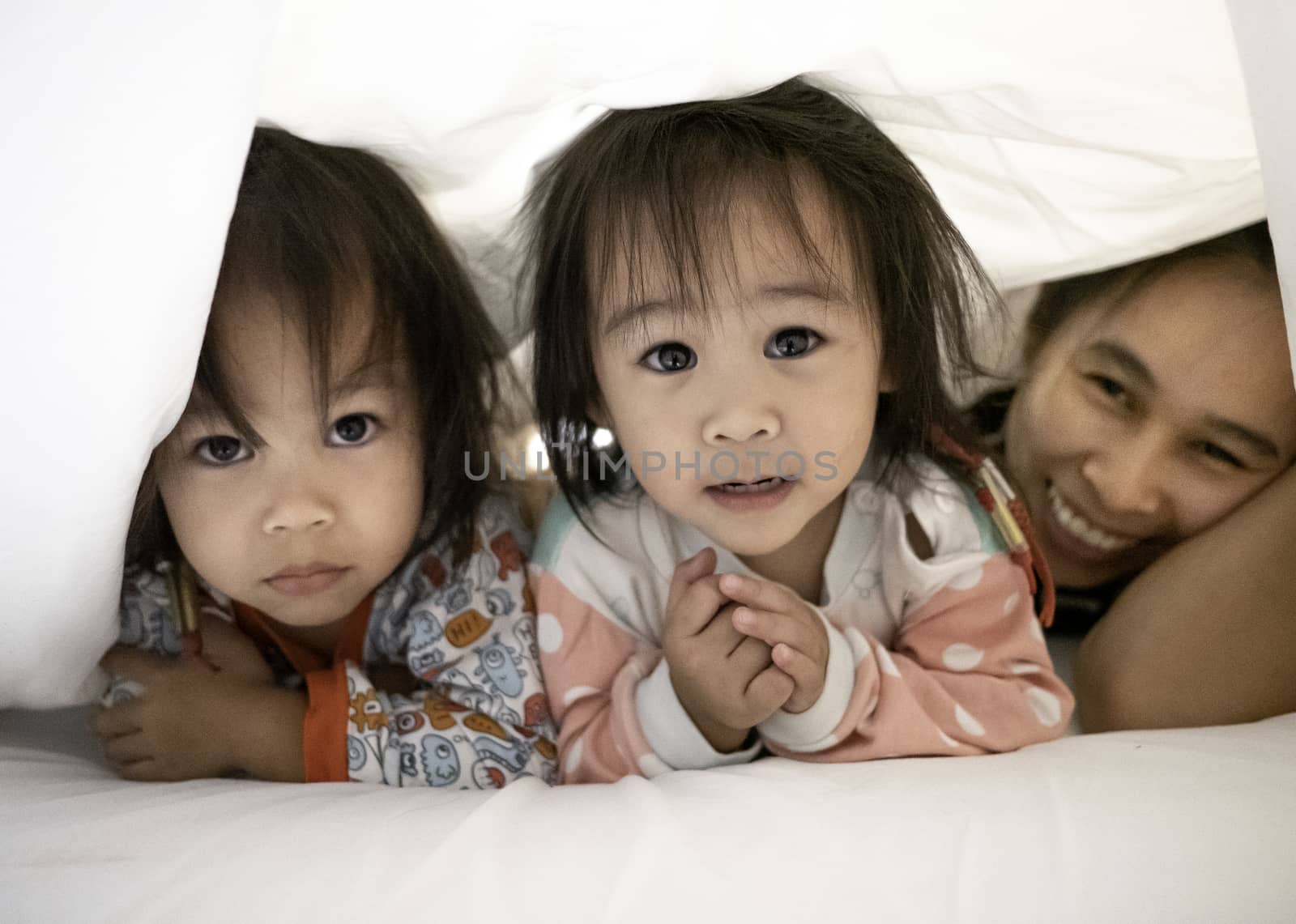 Portrait of Asian family lie about under a white blanket on the bed and looking camera. Relaxation time with family. by TEERASAK