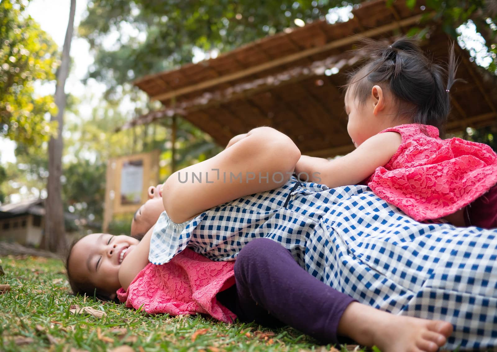 Asian little girl hugging her mother from the back; Pretend mother while lying on grass in the park.