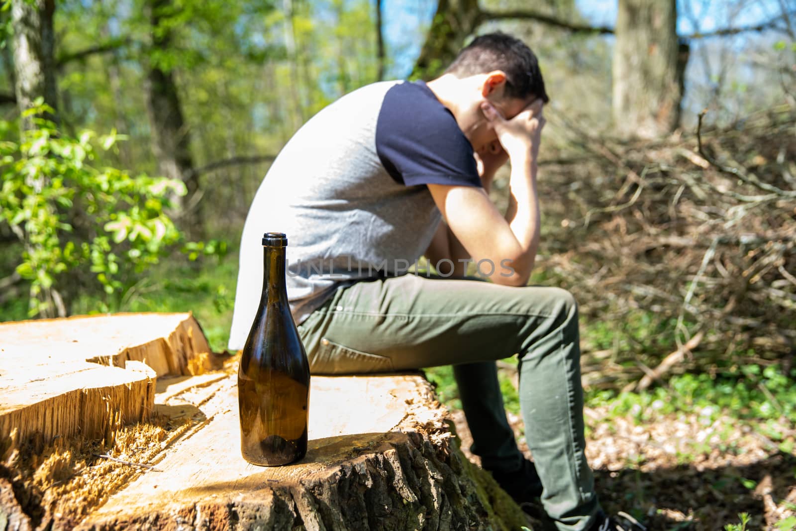 An unhappy man solves problems with alcohol. sad and alone with a bottle of alcohol in nature.