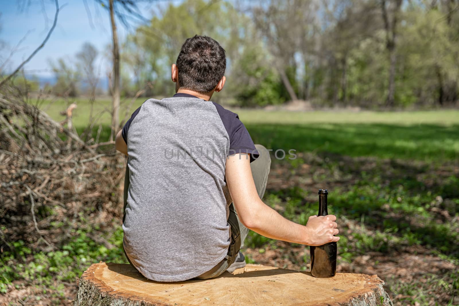 alcohol as a solution to a problem, a worried man with a bottle in his hand thinking about worries in the woods.