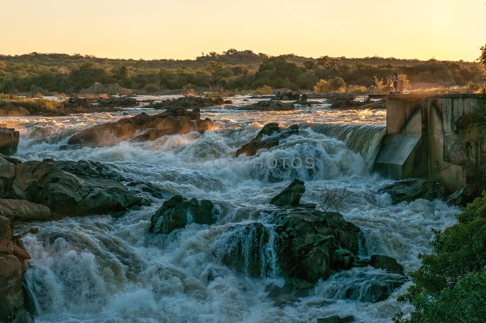 The top of the Ruacana waterfall in the Kunene River at sunset. An artist is visible. Angola is visible accross the river