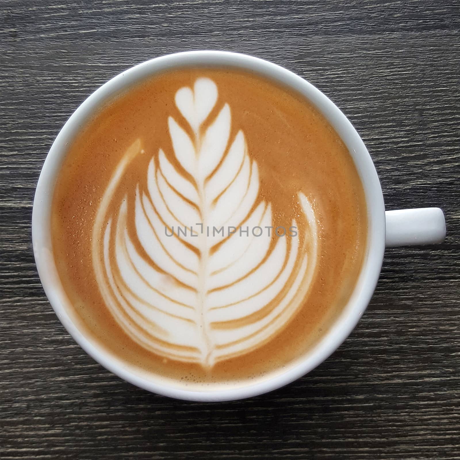 Top view of a mug of latte art coffee on timber background.