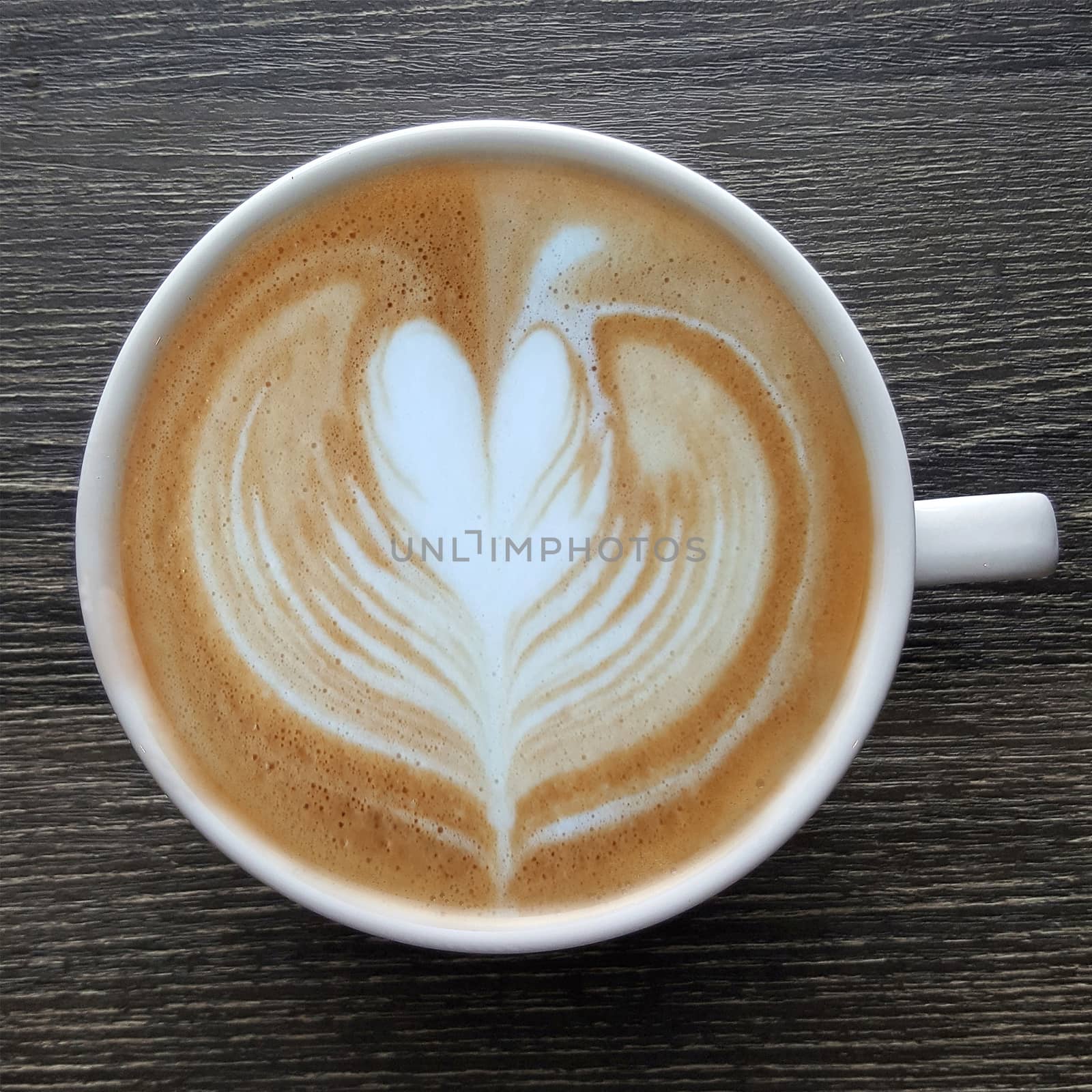 Top view of a mug of latte art coffee on timber background.