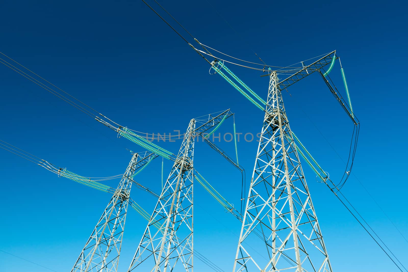 High voltage power lines with blue sky on the background, three electricity pylons