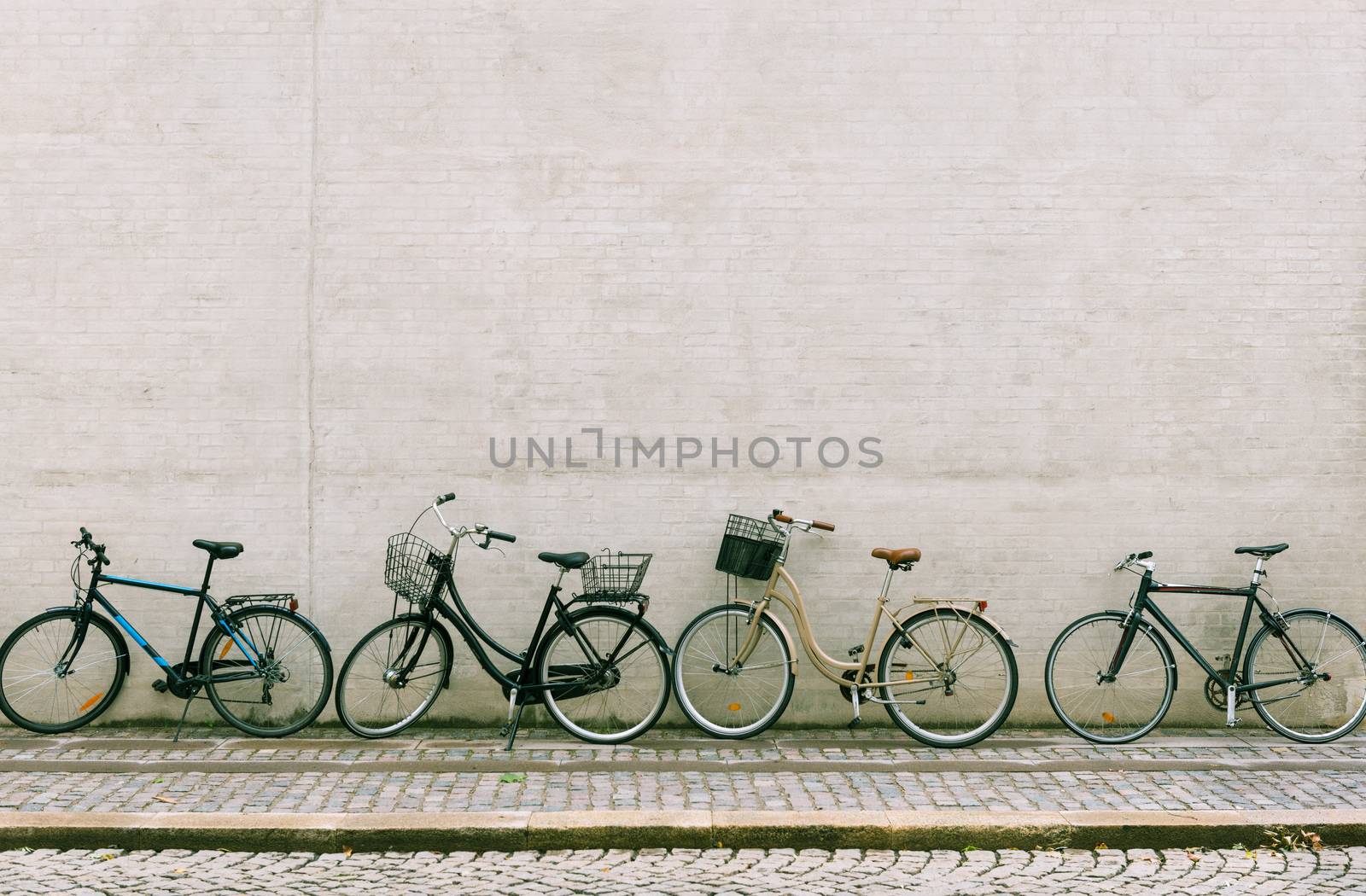 Four bicycles stand near a white brick wall. Several different bikes parked along an empty street in Copenhagen