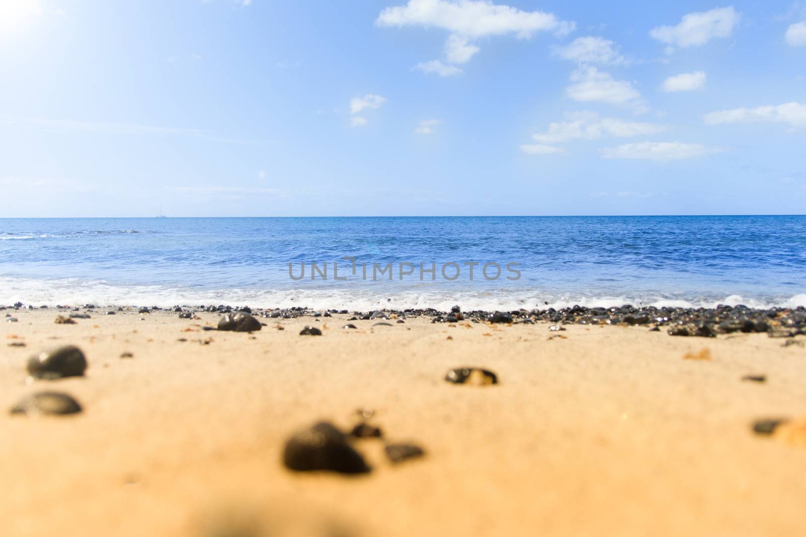 waves and blue waters. Beach with black stones and the sun.