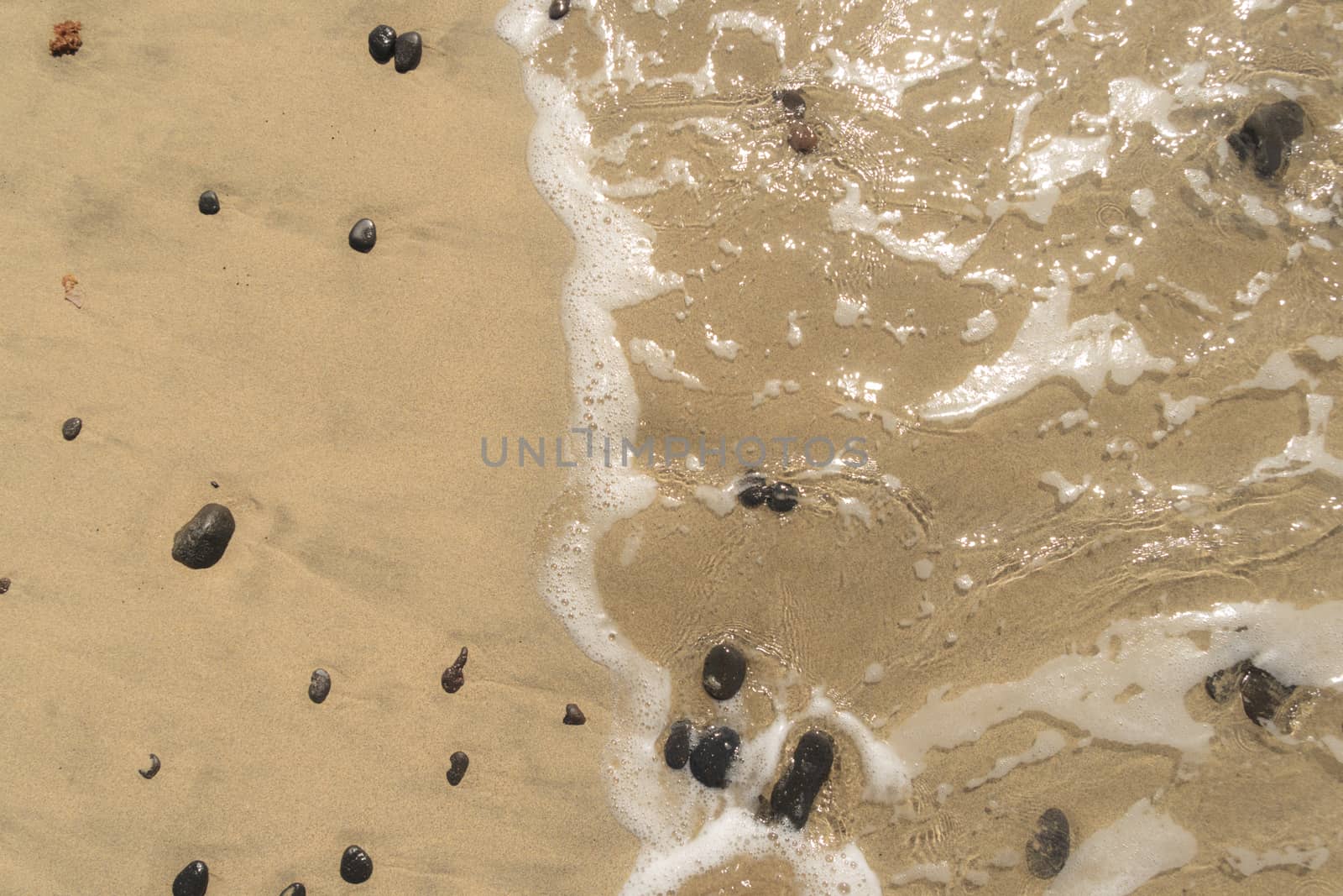 Black stones, sand and wave on the beach .