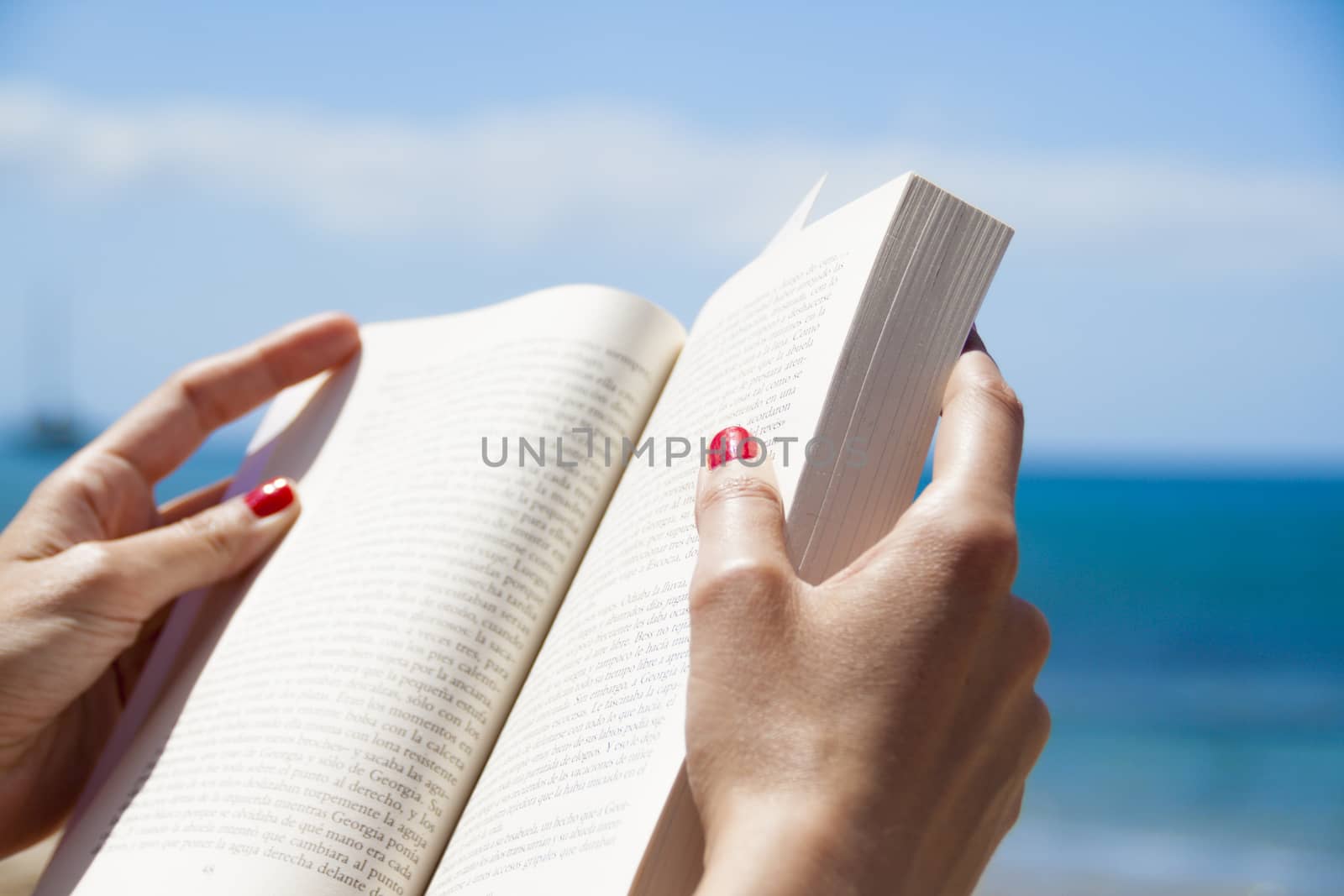 Woman hands holding and reading a book on the beach by tanaonte